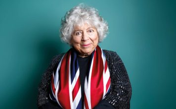 photo of Miriam Margolyes, draped in union jack flag on a green background smiling at the camera