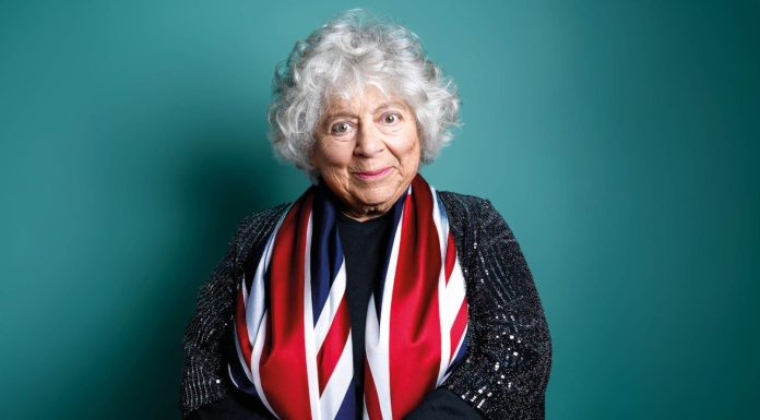 Miriam Margolyes Miriam Margolyes London 2026-photo of Miriam Margolyes, draped in union jack flag on a green background smiling at the camera