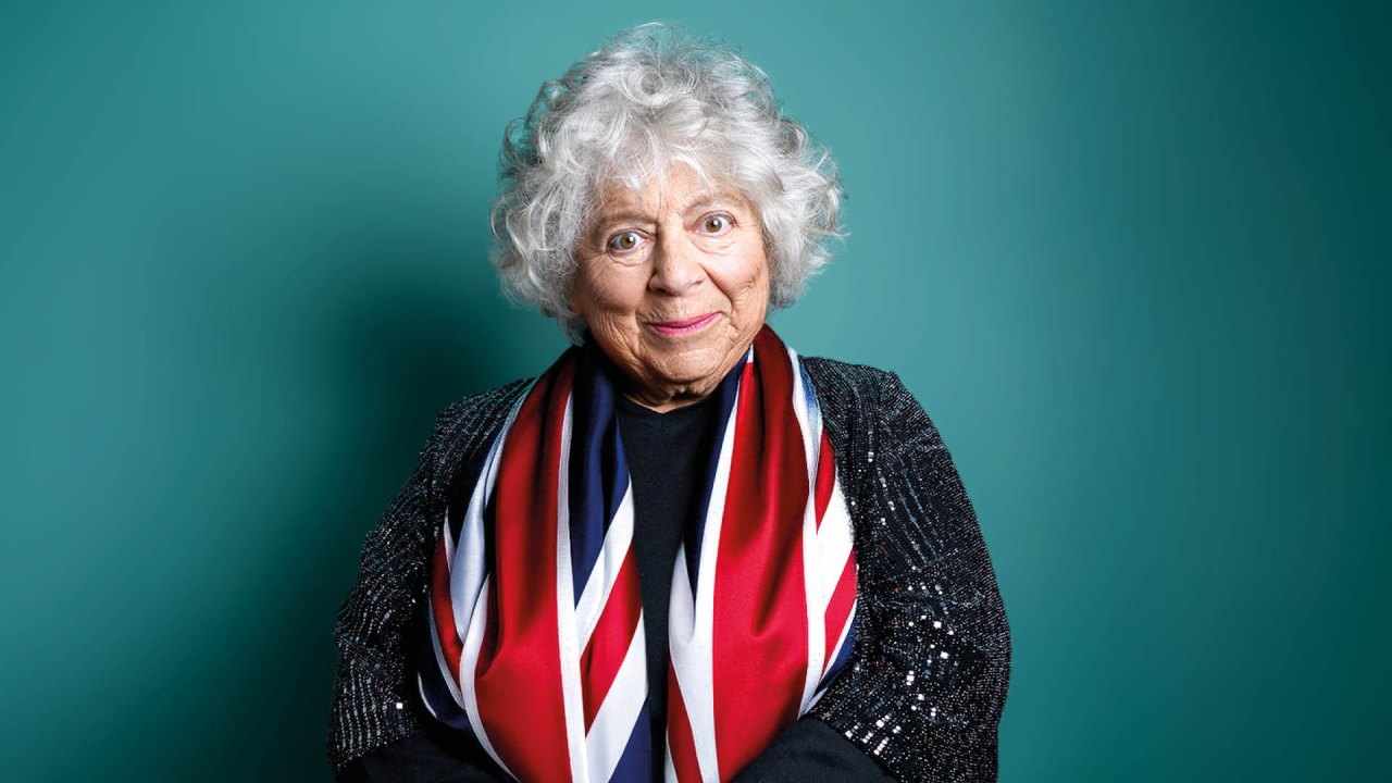 Miriam Margolyes photo of Miriam Margolyes, draped in union jack flag on a green background smiling at the camera